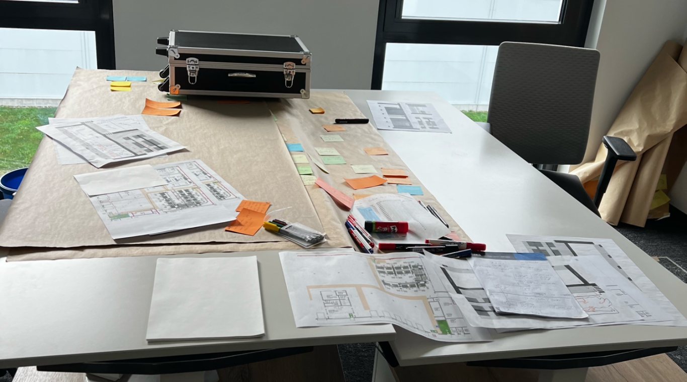 Arbeitstisch mit Layouts und Unterlagen Analyse von Materialfluss und Lagerlayout bei einem Logistikprojekt